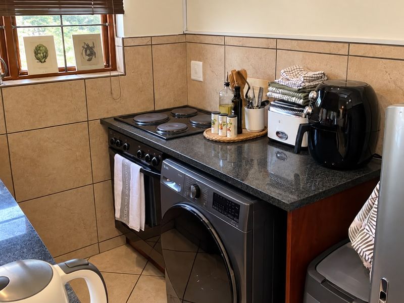 Compact kitchen featuring granite countertops, a built-in electric hob and oven, tiled backsplash, and an integrated washing machine.