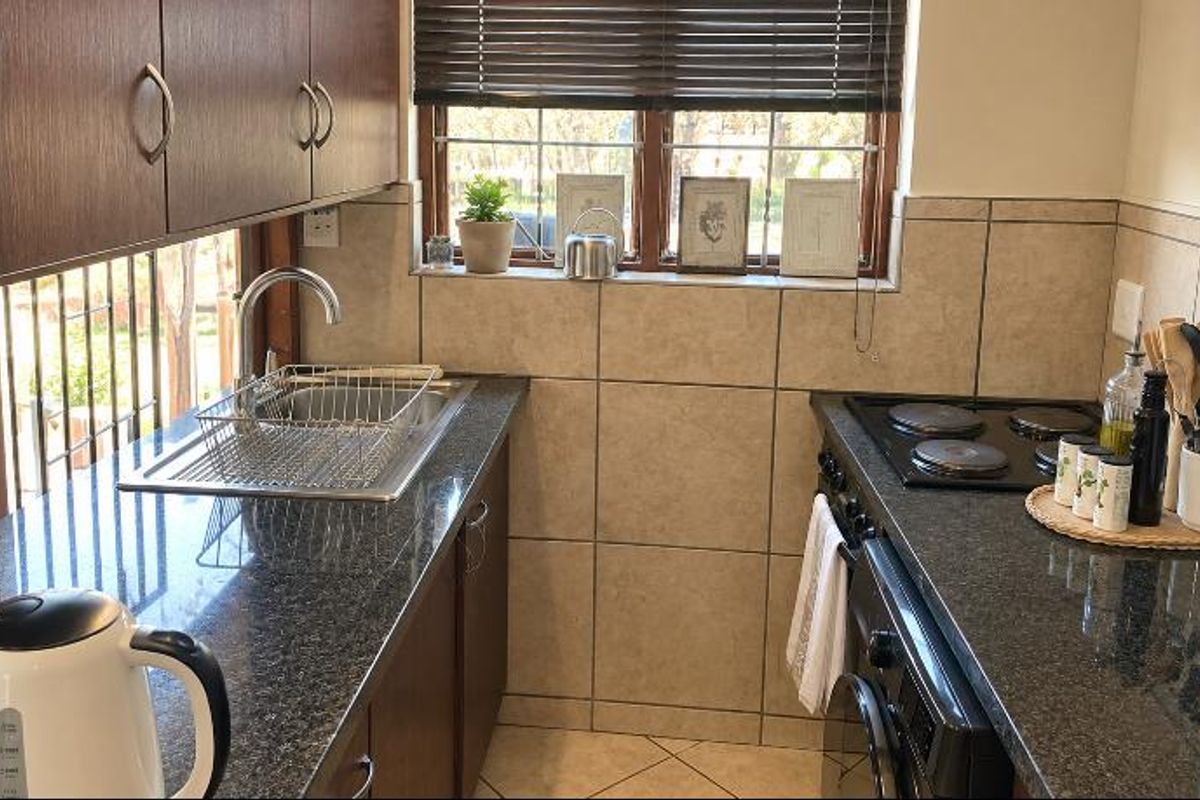 Compact kitchen featuring granite countertops, built-in cabinetry, a stainless steel sink, and an integrated electric hob and oven with tiled backsplash.