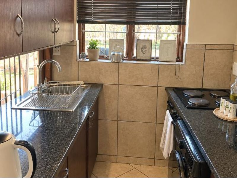 Compact kitchen featuring granite countertops, built-in cabinetry, a stainless steel sink, and an integrated electric hob and oven with tiled backsplash.