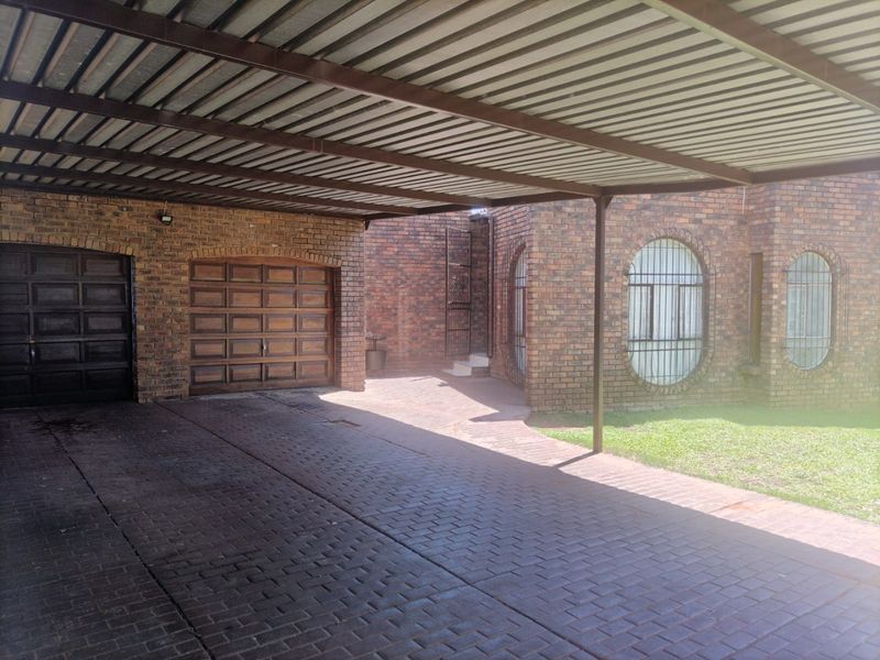 A well-maintained brick exterior featuring a spacious covered carport, paved driveway, and distinctive arched windows with security bars.