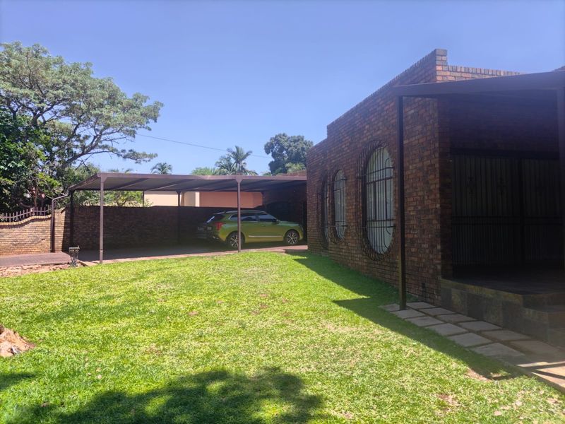 A front exterior view of a face brick house featuring a covered carport, security-barred windows, and a well-maintained lawn.