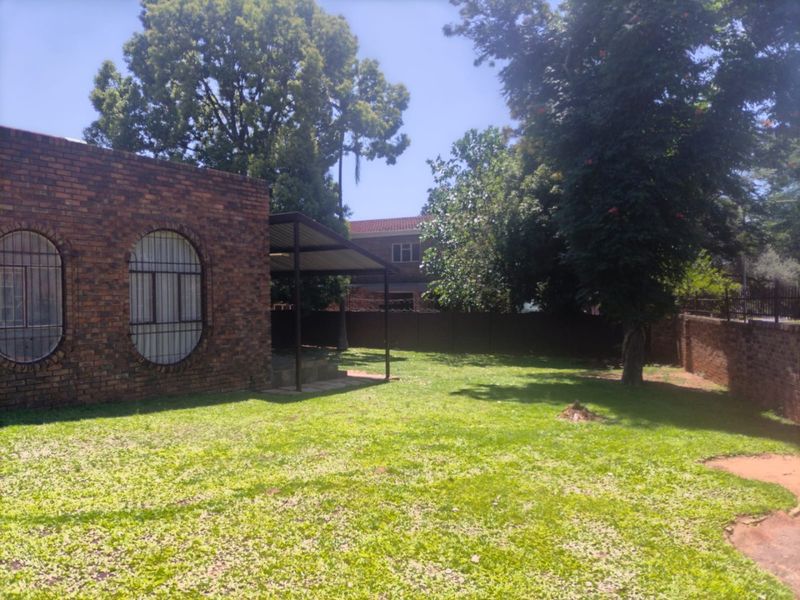 A spacious rear garden featuring a face brick exterior, a covered patio area, and established trees within a secure walled perimeter.