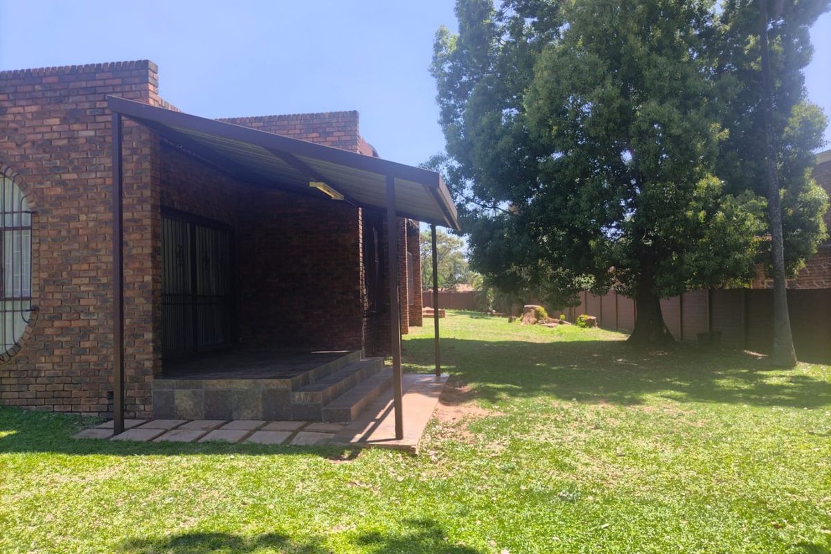 A rear view of the property featuring a face brick exterior, a covered patio area, and a spacious garden with mature trees.