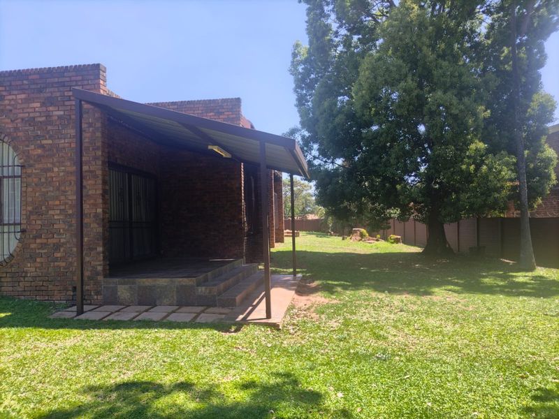 A rear view of the property featuring a face brick exterior, a covered patio area, and a spacious garden with mature trees.