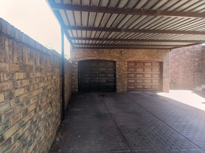 A double garage featuring brick construction, wooden garage doors, and a covered carport area with paved driveway.