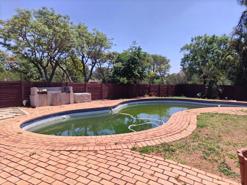 Outdoor pool area featuring a swimming pool, brick paving, and a built-in braai, enclosed by a perimeter fence.