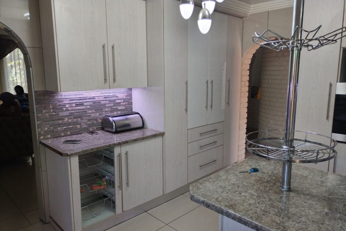 Modern kitchen featuring light wood-grain cabinetry, granite countertops, a central island, and a stylish mosaic tile backsplash with integrated under-cabinet lighting.