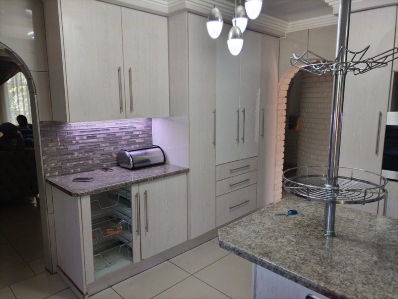 Modern kitchen featuring light wood-grain cabinetry, granite countertops, a central island, and a stylish mosaic tile backsplash with integrated under-cabinet lighting.