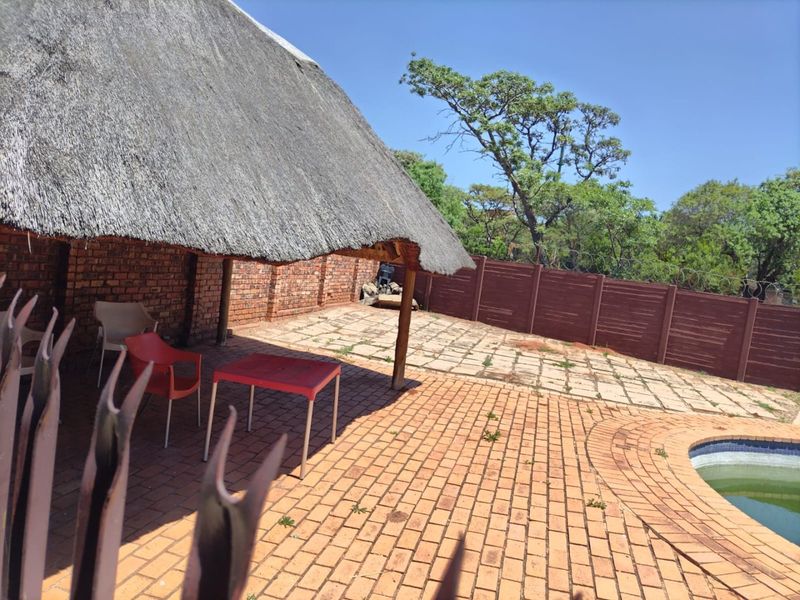 Outdoor patio area featuring a traditional thatch roof, brick paving, and direct access to a swimming pool, enclosed by a perimeter wall.
