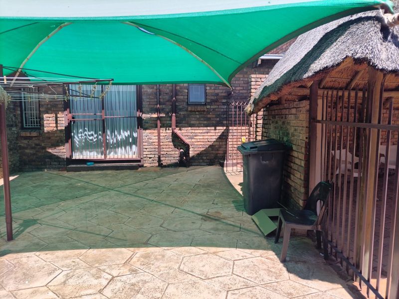 A paved outdoor patio area featuring a thatch roof structure and a green shade sail, providing a functional space for outdoor living.