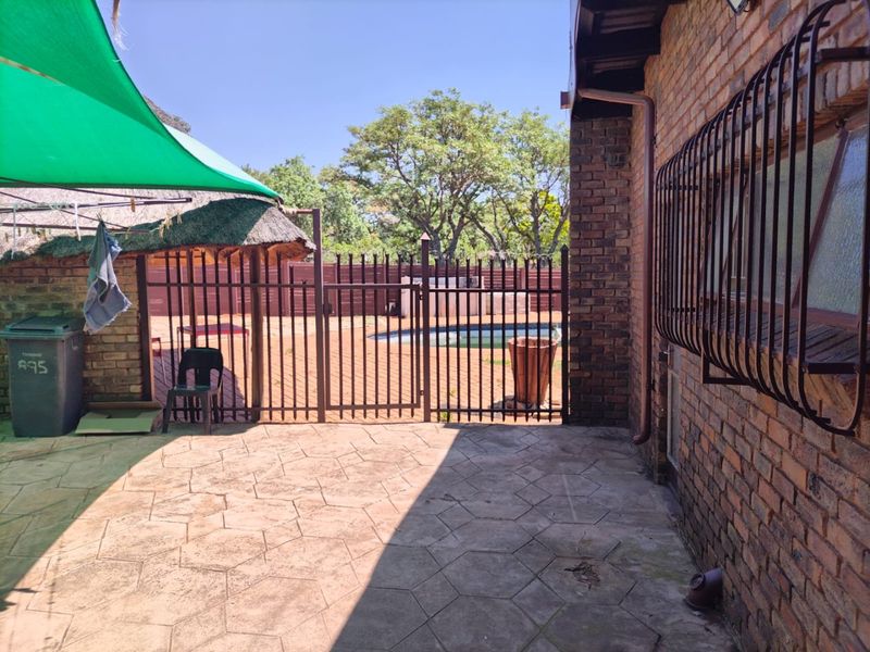 Outdoor pool area featuring brick paving, security fencing, and a thatched structure, providing a functional space for outdoor recreation.