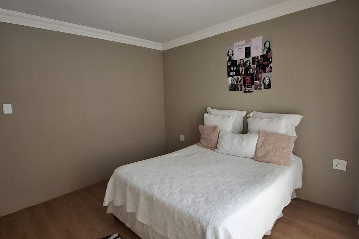 A neutrally painted bedroom featuring laminate flooring, coved ceiling cornicing, and a central ceiling light fixture.