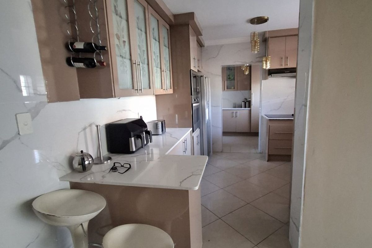 A well-appointed kitchen featuring modern cabinetry, stone countertops, marble-look wall finishes, and a functional layout with an adjoining scullery area.