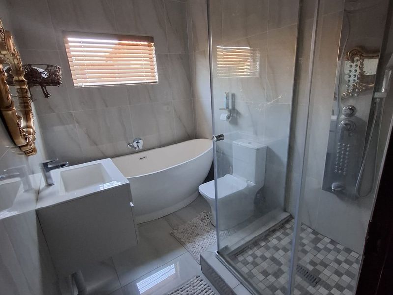 Modern bathroom featuring a freestanding bathtub, glass-enclosed shower with mosaic tiling, wall-mounted vanity, and neutral wall tiles.