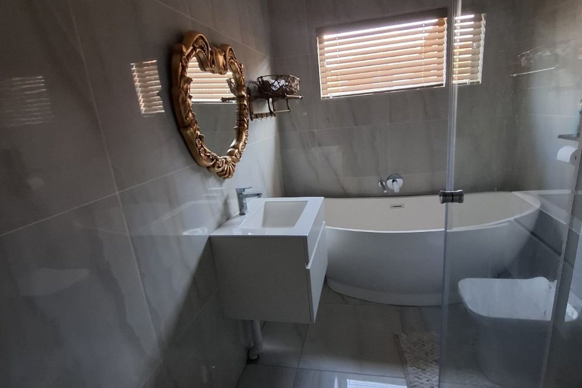 Modern bathroom featuring a sleek freestanding bathtub, wall-mounted vanity, glass shower enclosure, and neutral floor-to-ceiling tiling.