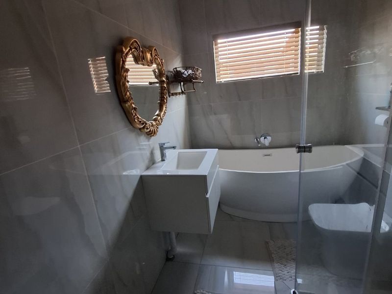 Modern bathroom featuring a sleek freestanding bathtub, wall-mounted vanity, glass shower enclosure, and neutral floor-to-ceiling tiling.