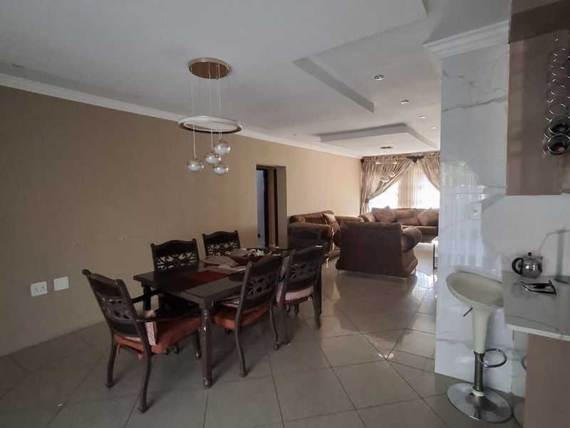 Spacious open-plan living and dining area featuring large format floor tiles, a modern dropped ceiling, and a marble-finished breakfast bar.
