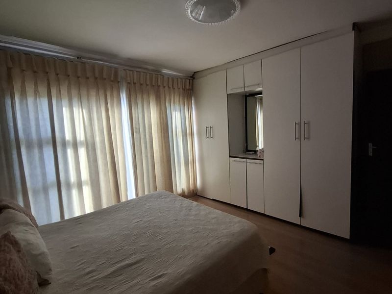 A well-lit bedroom featuring extensive built-in cupboards with integrated vanity mirror and durable laminate flooring.