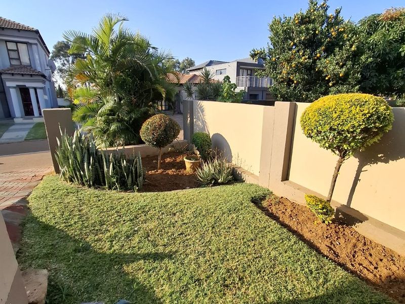 A well-maintained front garden area featuring manicured lawn, established shrubs, and a solid boundary wall, providing a neat and welcoming street-facing entrance.