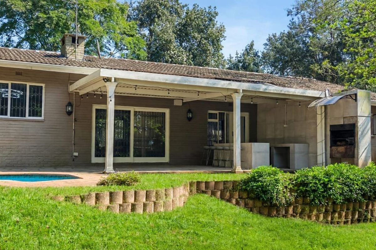 Rear view of the house featuring a covered patio with a built-in braai, swimming pool, and landscaped garden with a retaining wall.