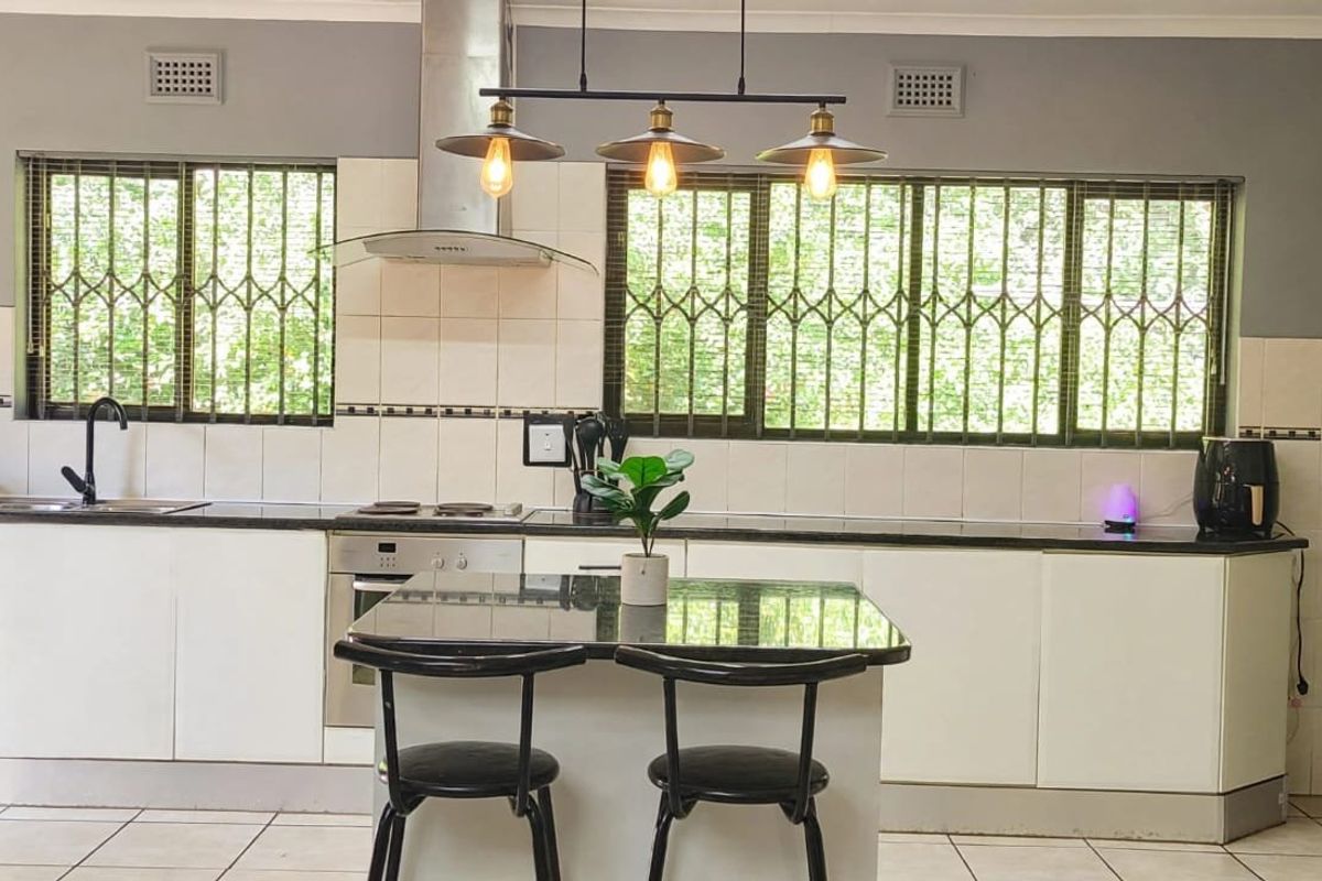 A functional kitchen featuring white cabinetry, granite countertops, a built-in oven with hob, and a tiled backsplash with security bars on the windows.