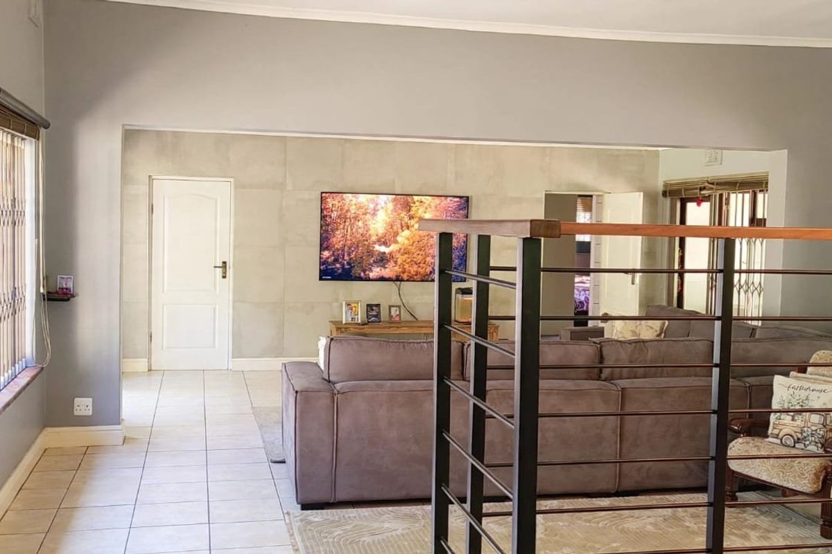 Spacious living area featuring tiled flooring, a modern feature wall, and a metal staircase railing, providing an open and functional layout.