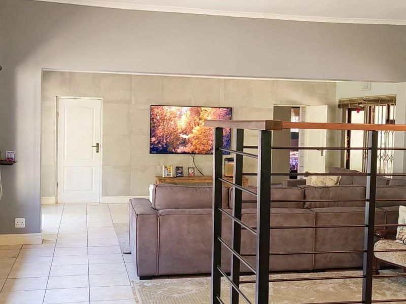 Spacious living area featuring tiled flooring, a modern feature wall, and a metal staircase railing, providing an open and functional layout.