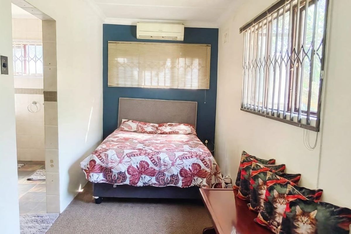 A functional bedroom featuring carpeted flooring, an air conditioning unit, and a security gate on the window, with an adjoining bathroom area.