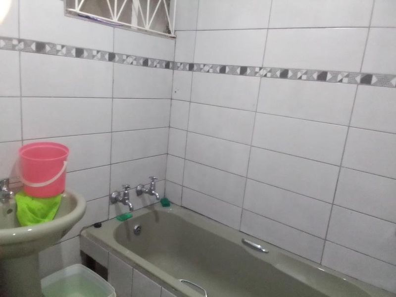 A functional bathroom featuring a pedestal basin, bathtub, and tiled walls. The space would benefit from modern updates to fixtures and finishes.