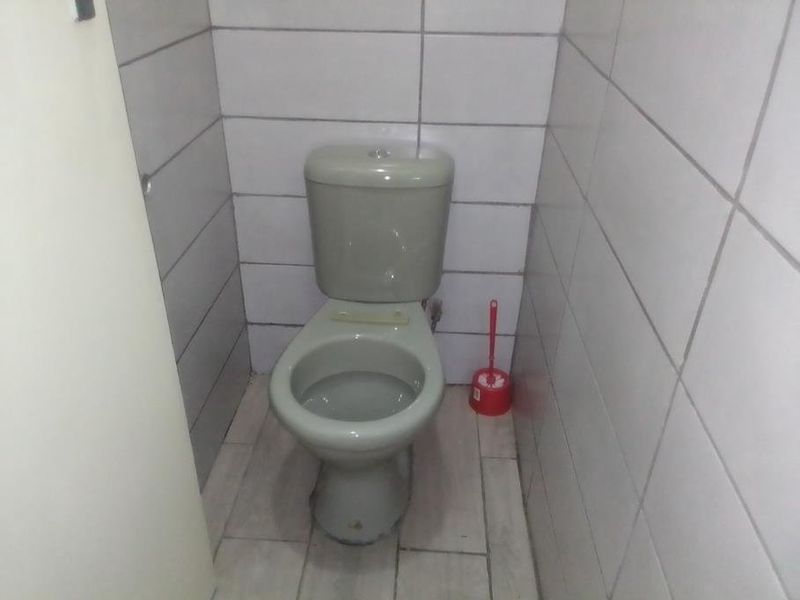 A small, functional bathroom featuring a standard toilet with tiled walls and flooring, requiring cosmetic updates to improve its overall condition.