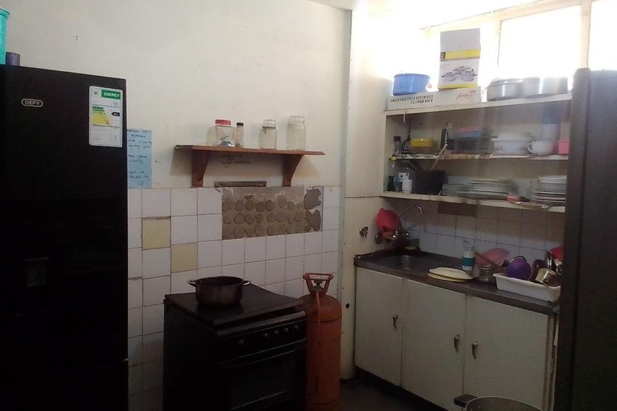 A dated kitchen featuring basic cabinetry, a stainless steel sink, and a tiled splashback with visible wall damage requiring repair and modernization.
