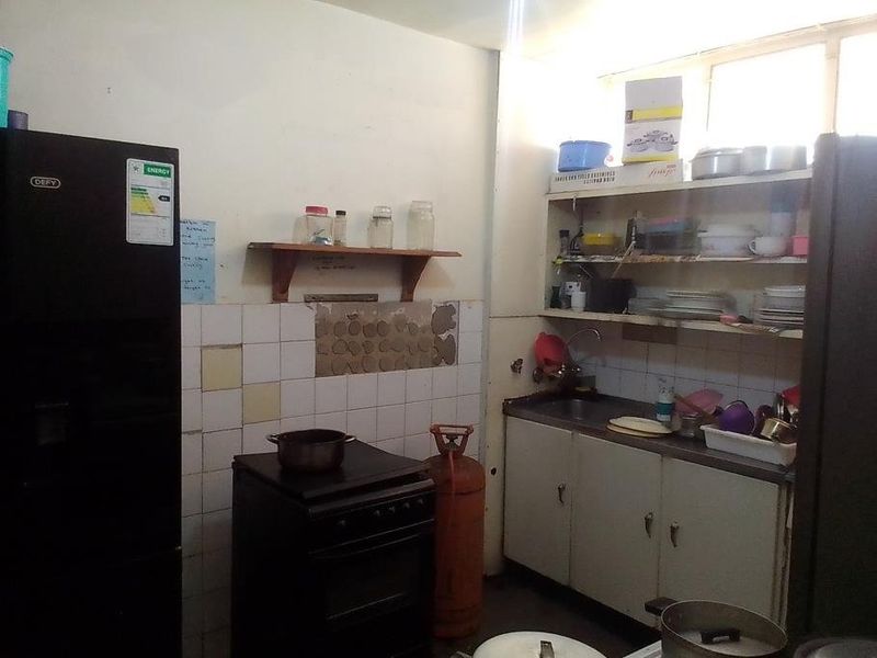 A dated kitchen featuring basic cabinetry, a stainless steel sink, and a tiled splashback with visible wall damage requiring repair and modernization.