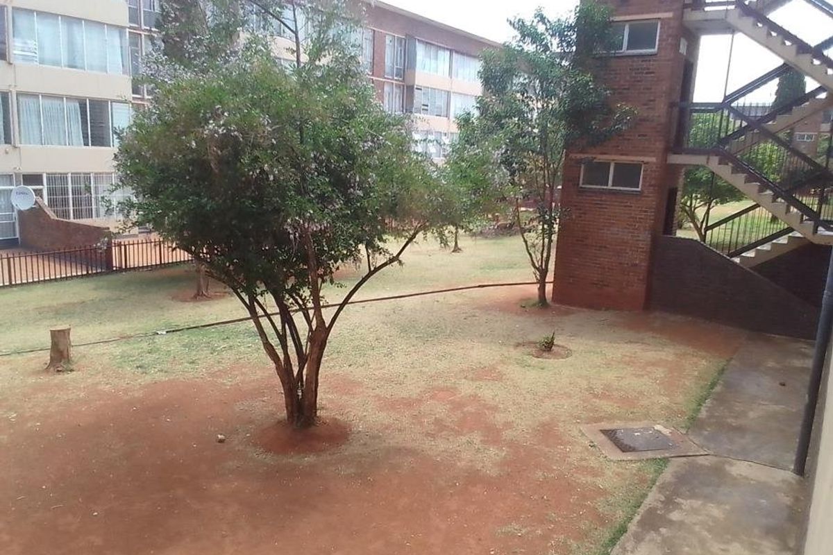 A view of the communal garden area featuring a brick stairwell, concrete pathways, and established trees within an apartment complex setting.