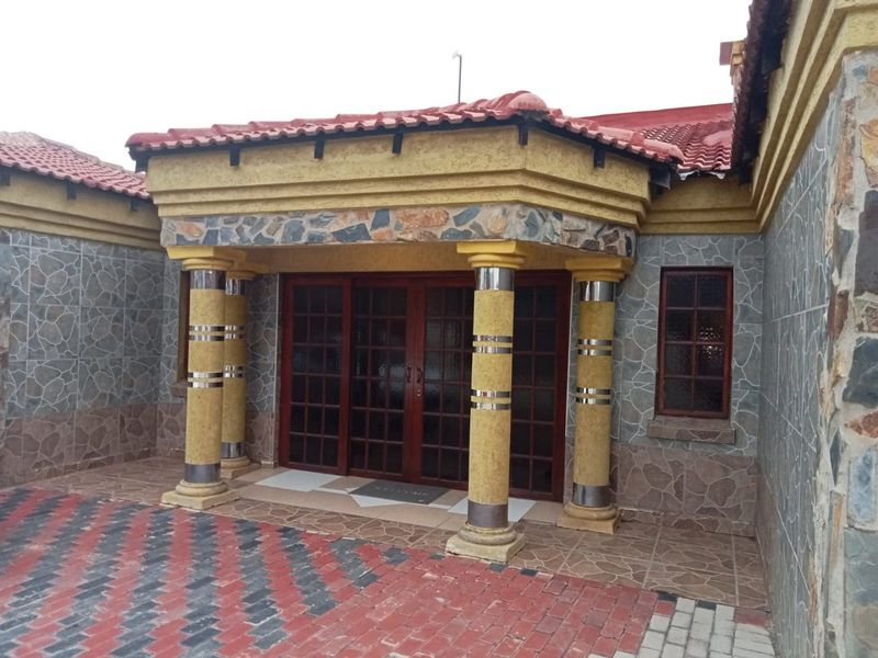 Front entrance of the house featuring stone cladding, decorative columns, and a paved driveway leading to timber-framed glass doors.