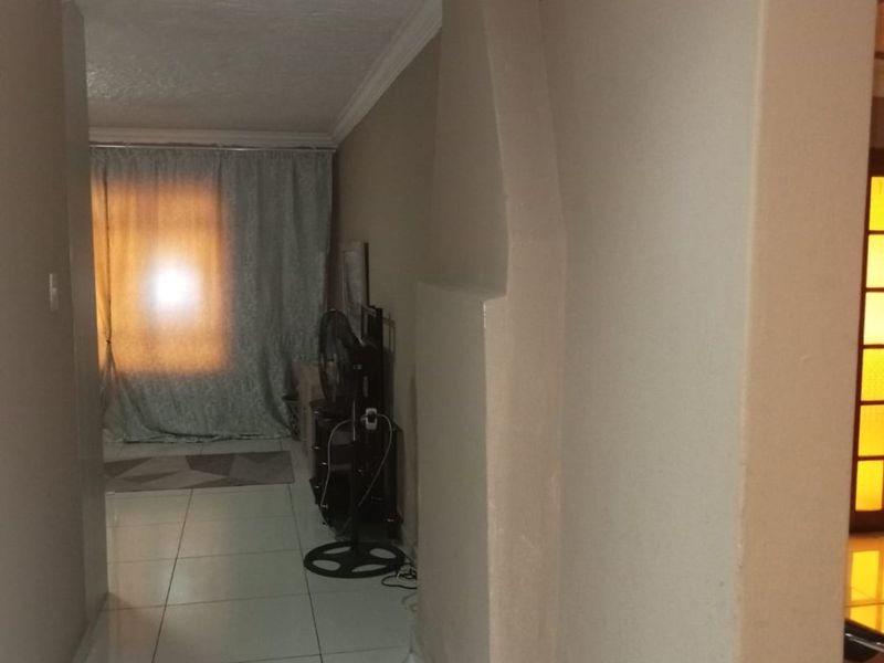 A narrow hallway featuring tiled flooring and decorative ceiling cornicing, leading towards a naturally lit living area.