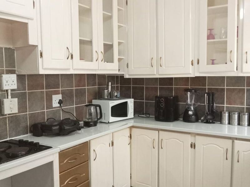 A functional kitchen featuring white cabinetry with glass-fronted upper units, dark tiled backsplash, and tiled flooring, providing a classic layout ready for modern updates.