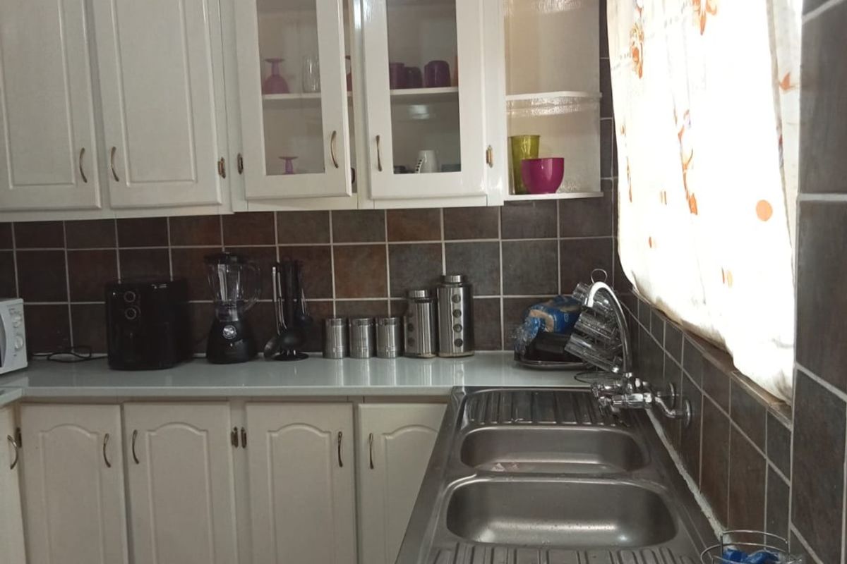 A functional kitchen featuring white cabinetry, a double bowl stainless steel sink, and dark tiled splashbacks.