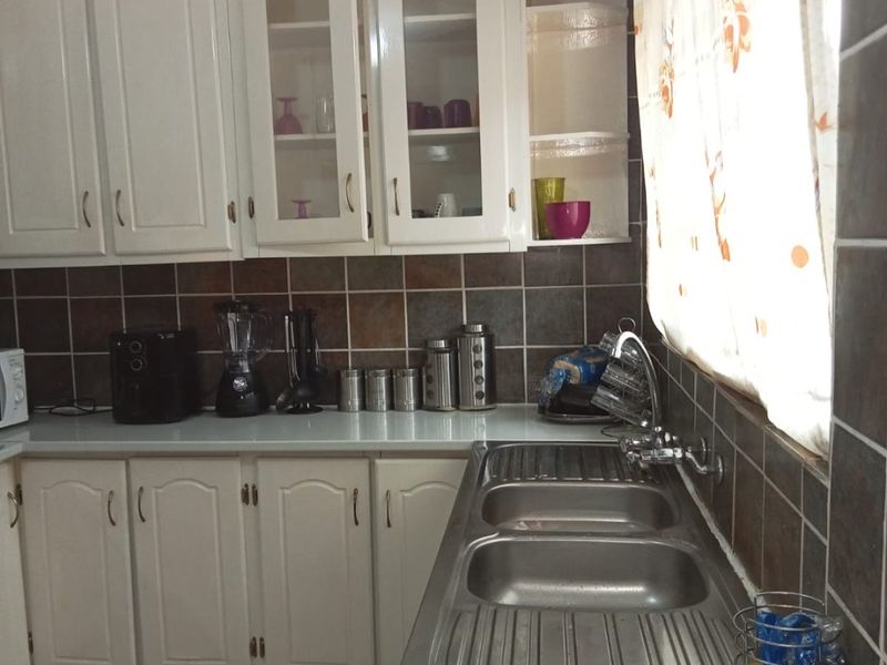 A functional kitchen featuring white cabinetry, a double bowl stainless steel sink, and dark tiled splashbacks.