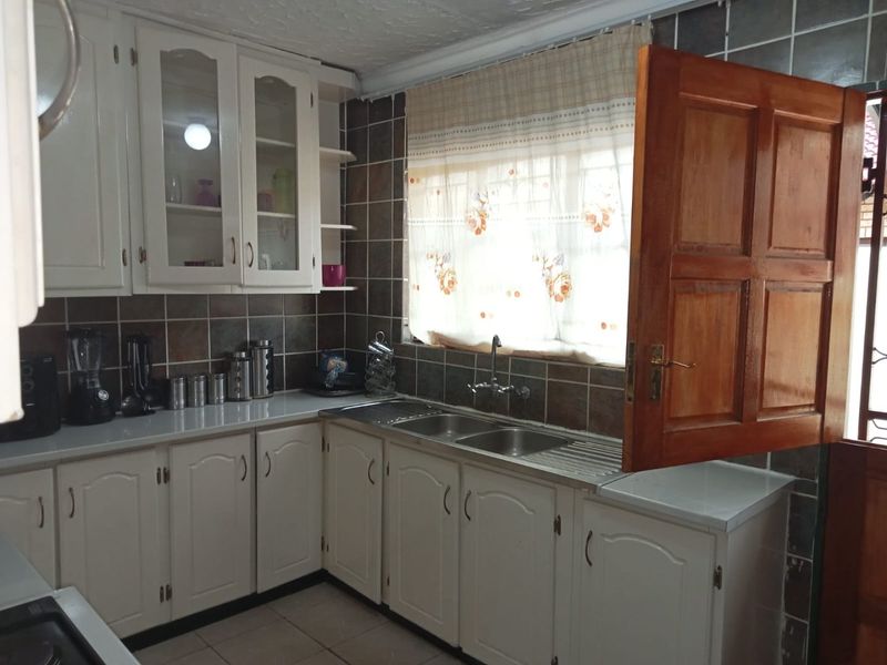 A functional kitchen featuring white cabinetry, a double stainless steel sink, and dark tiled splashbacks, offering a classic layout with ample storage space.