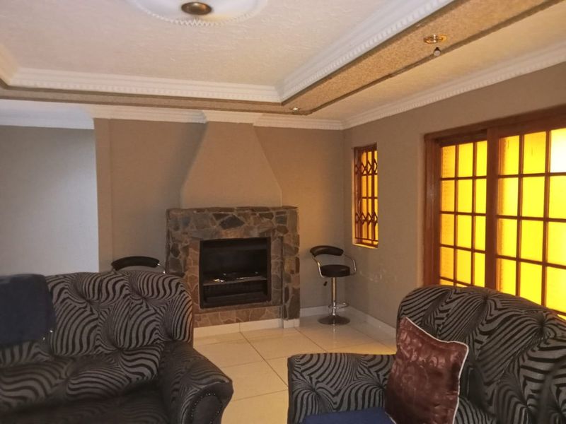A living room featuring a stone fireplace, tiled flooring, and decorative ceiling cornices, with access to the outdoors via a sliding glass door.