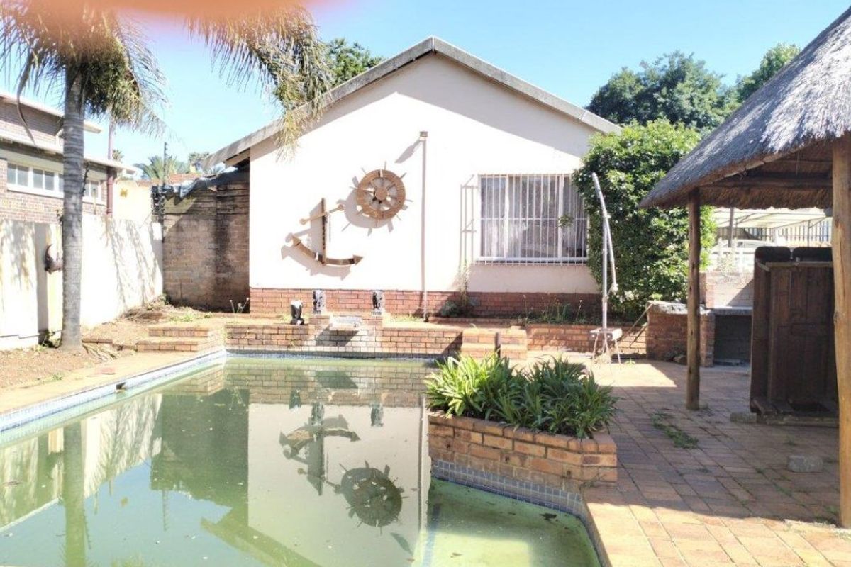 Outdoor pool area featuring a swimming pool, brick paving, and a thatched lapa, offering potential for a revitalized entertainment space.