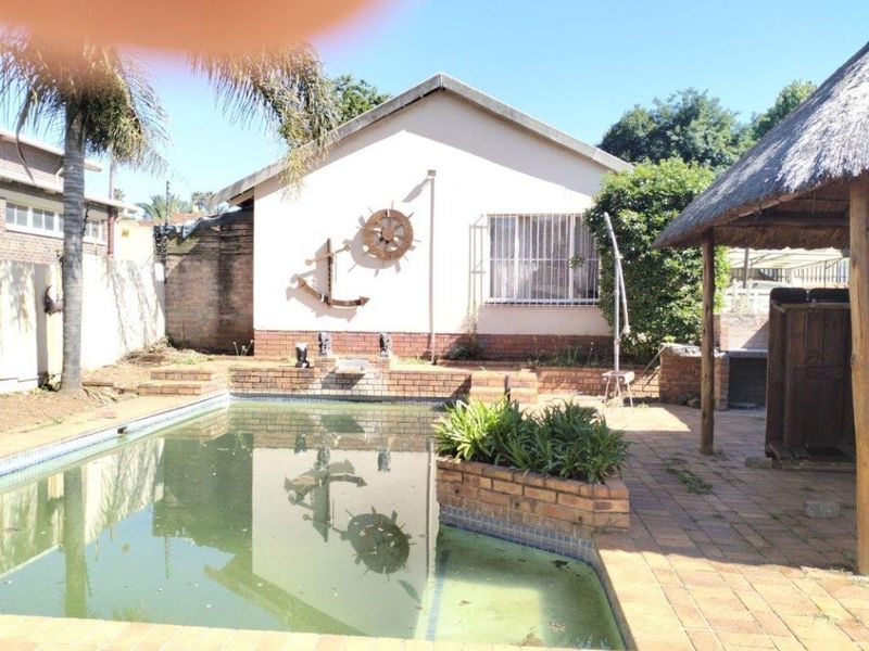 Outdoor pool area featuring a swimming pool, brick paving, and a thatched lapa, offering potential for a revitalized entertainment space.