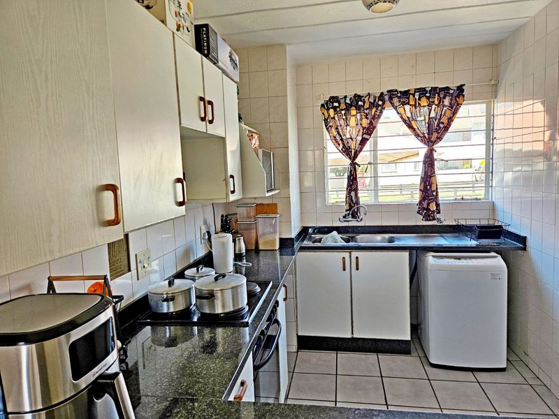 A functional kitchen featuring granite countertops, built-in cabinetry, a double basin sink, and tiled finishes throughout.