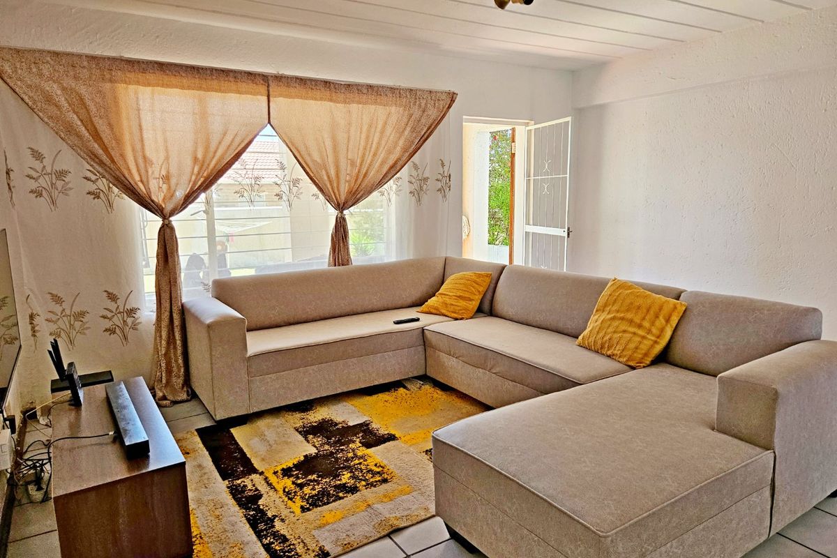 A comfortable living room featuring tiled flooring, a large window for natural light, and direct access to an outdoor area via a security gate.