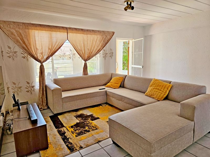 A comfortable living room featuring tiled flooring, a large window for natural light, and direct access to an outdoor area via a security gate.