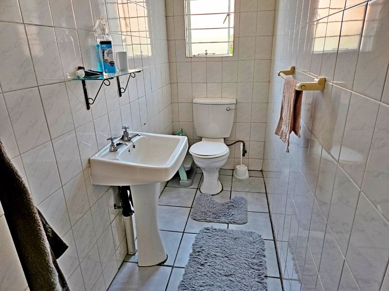 A functional bathroom featuring a pedestal basin, toilet, and full-height ceramic wall tiling with a window for natural light.