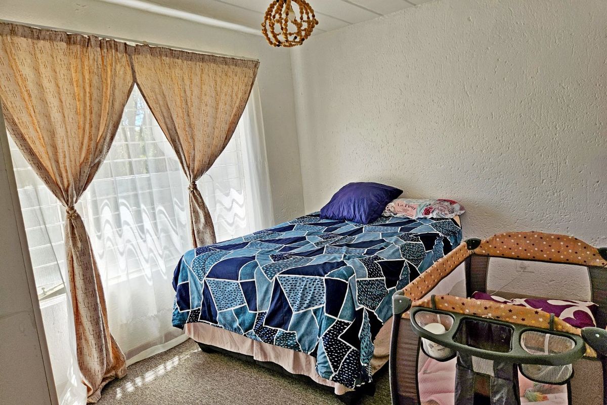 A functional bedroom featuring textured walls, carpeted flooring, and a large window allowing natural light into the space.