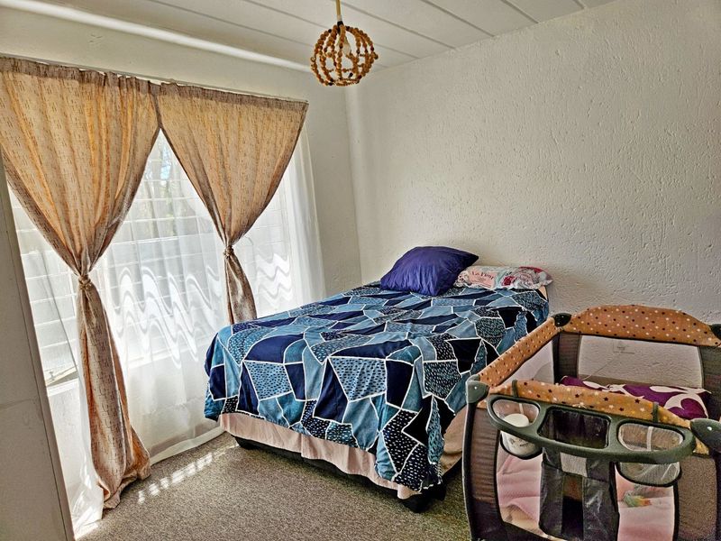 A functional bedroom featuring textured walls, carpeted flooring, and a large window allowing natural light into the space.