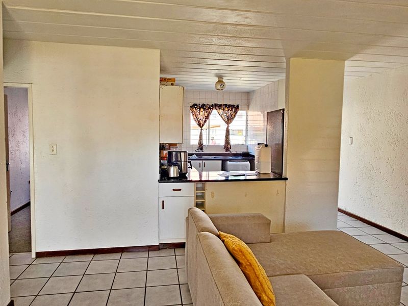 Open plan living area featuring a compact kitchen with tiled flooring and dated cabinetry, offering potential for modern renovation.
