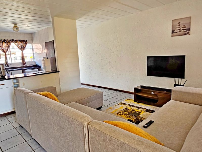 Open plan living area featuring tiled flooring, textured walls, and a kitchen breakfast bar, creating a functional and connected living space.